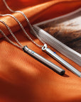Two stainless steel bullet vibrators displayed on an orange fabric beside a magazine, showcasing their discreet design as a bullet vibrator, mini vibrator, bullet sex toy, and vibrator necklace