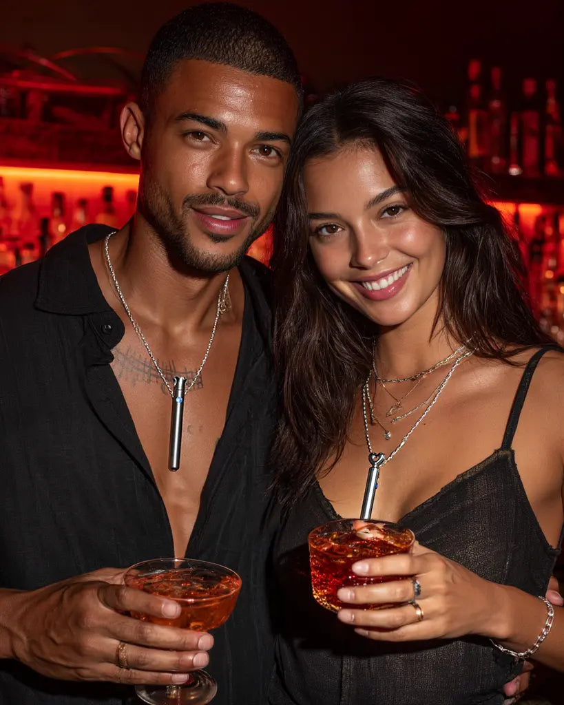 A man and woman standing together at a bar, both wearing Lumea bullet vibrator necklaces, smiling at the camera and enjoying discreet fun.