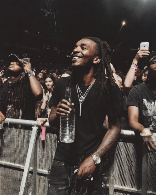 A Black person standing in a concert crowd, wearing the Lumea bullet vibrator necklace, a discreet mini vibrator and bullet sex toy, enjoying pleasure anywhere